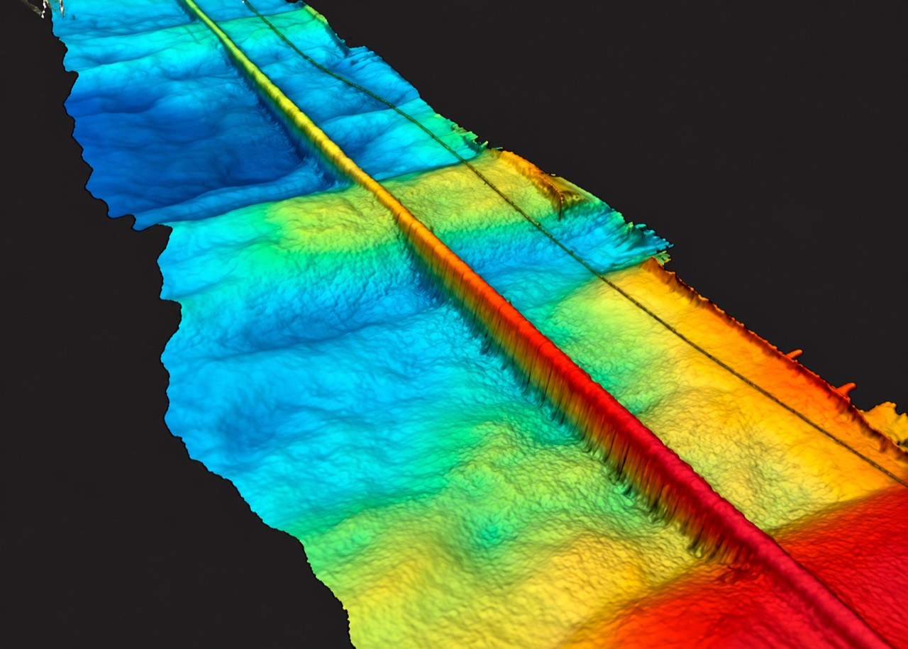 Illustrative bathymetric seabed surface in blue, cyan, yellow and red, with linear subsea infrastructure.